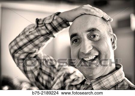 Picture - Close-up of the face of a 40-year-old Caucasian man, smiling and with positive attitude, with one hand on his head and wearing plaid shirt.. Fotosearch