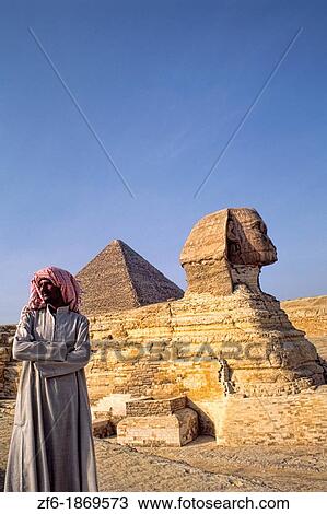 Stock Image - Close up of the famous Sphinx and the Pyramids of Giza in Egypt with local Arab man portrait. Fotosearch