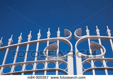 Stock Photo - Close-up of white painted iron gates against a blue sky, Terrebonne, Quebec, Canada. Fotosearch