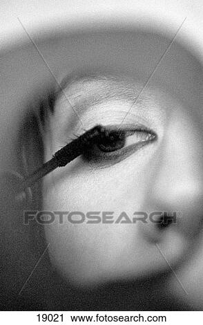 Stock Image - Close up of woman applying mascara in a pocket mirror. Fotosearch
