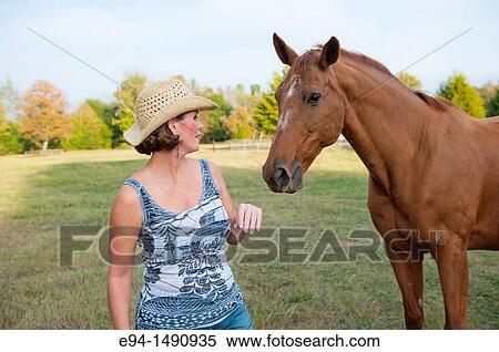 Close up portrait of a 52 year old blonde woman wearing a tank top and a straw hat interacting with a horse in a pasture. View Large Photo Image Stock Photography - Close up portrait of a 52 year old blonde woman wearing a tank top and a straw hat interacting with a horse in a pasture.. Fotosearch