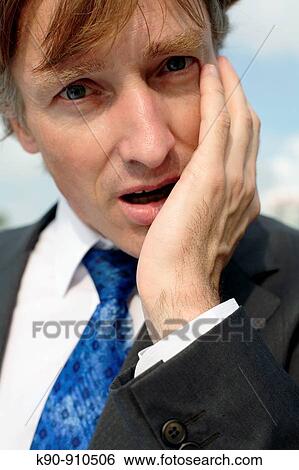 Stock Photograph - Close-up portrait of of young, caucasian business man in grey suit looking very worried into the camera, with one hand at his cheek, Hong Kong, China, Asia. Fotosearch