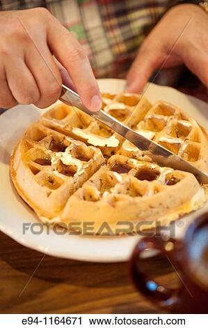 Stock Image - Close up view of a man cutting a breakfast waffle with a knife in a restaurant.. Fotosearch
