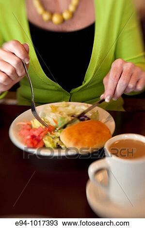 Stock Image - close view of a woman cutting up a tossed salad in a restaurant, coffee cup also on the table. Fotosearch