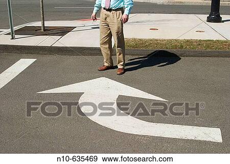 Stock Photo - Close_up of a man standing in front of a traffic arrow that points towards him. Fotosearch