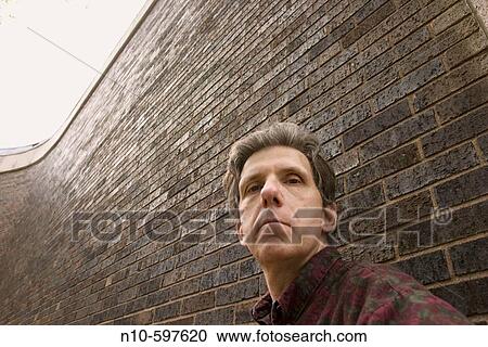 Stock Image - Close_up of a middle_age man standing against a brick building. Fotosearch