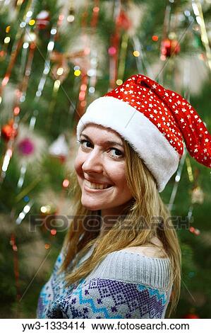Picture - closeup of pretty girl in christmas hat against decorated xmas tree. Fotosearch