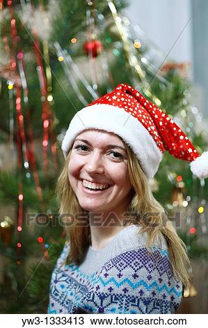 Stock Image - closeup of pretty girl in christmas hat against decorated xmas tree. Fotosearch