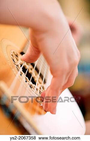 Stock Photo - Closeup of womans hand playing on wooden acoustic guitar.. Fotosearch