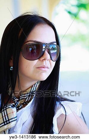Stock Photograph - Closeup portrait of a beautiful 20-25 years happy woman in blur background outdoors with sunglasses. Fotosearch
