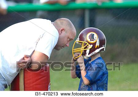 Stock Image - Coach talking to kid at football practive about game and learning rules. Fotosearch