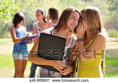 Stock Image - College students in two groups. Selective focus. In the foreground two friends whispering a secret. Fotosearch