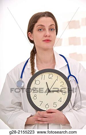 Concept image, Young woman in white overall, doctor or nurse, holding a clock in front of her View Large Photo Image Stock Image - Concept image, Young woman in white overall, doctor or nurse, holding a clock in front of her. Fotosearch