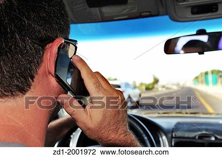 Stock Image - Concept photo of a male driver speaks on a mobile phone while driving.. Fotosearch