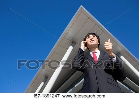 Confident young Asian businessman standing outside his office building View Large Photo Image Stock Photo - Confident young Asian businessman standing outside his office building. Fotosearch