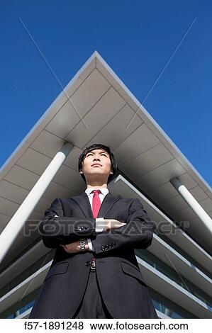 Confident young Asian businessman standing outside his office building View Large Photo Image Stock Photo - Confident young Asian businessman standing outside his office building. Fotosearch