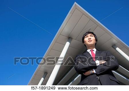 Confident young Asian businessman standing outside his office building View Large Photo Image Stock Photo - Confident young Asian businessman standing outside his office building. Fotosearch