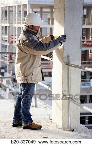 Stock Photo - Construction worker measuring, personal protective equipment, housing construction, concrete skeleton. Fotosearch
