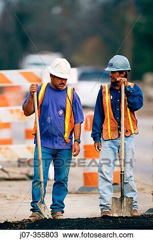 Stock Image - Construction workers leaning on shovels. Texas. USA.. Fotosearch