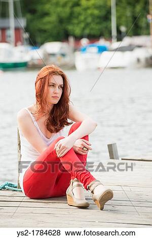 Contemplating young woman sitting on a jetty View Large Photo Image Stock Photo - Contemplating young woman sitting on a jetty. Fotosearch