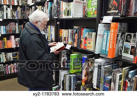Stock Image - Cork, County Cork, Ireland Elderly man reading book in Waterstone's book store. Fotosearch