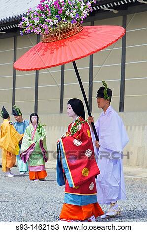 Stock Image - Costumed participants in the parade, some carrying red parasols for ladies walking beside them with the Imperial Palace in the background. Fotosearch