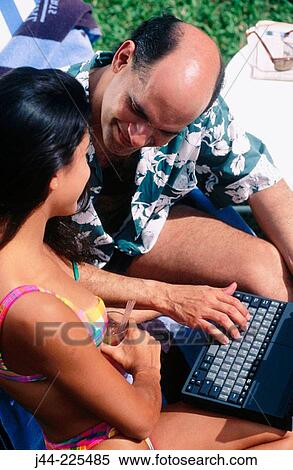Stock Photography - Couple by the pool with laptop computer. Fotosearch
