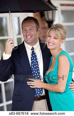 Stock Photo - Couple dressed up standing under an umbrella. Fotosearch