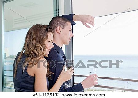 Stock Image - Couple drinking champagne looking at the sea at home. Fotosearch