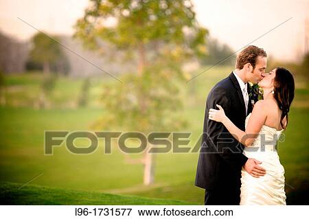 Stock Photo - couple embracing and kissing after ceremony on golf course green. Fotosearch