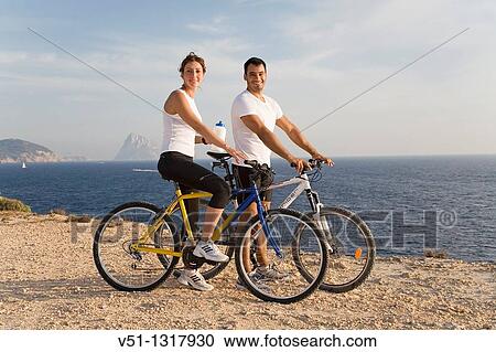 Couple enjoying the views in a cliff with their bikes and smiling at camera View Large Photo Image Stock Image - Couple enjoying the views in a cliff with their bikes and smiling at camera. Fotosearch