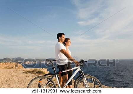 Stock Image - Couple enjoying the views in a cliff with their bikes. Fotosearch