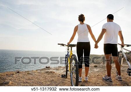 Stock Image - Couple enjoying the views in a cliff with their bikes. Fotosearch