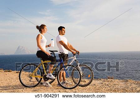 Couple enjoying the views in a cliff with their bikes View Large Photo Image Stock Image - Couple enjoying the views in a cliff with their bikes. Fotosearch