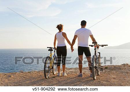 Stock Image - Couple enjoying the views in a cliff with their bikes. Fotosearch
