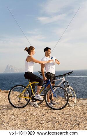 Stock Photo - Couple enjoying the views in a cliff with their bikes. Fotosearch
