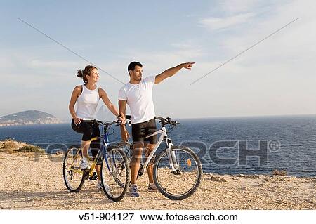 Couple enjoying the views in a cliff with their bikes View Large Photo Image Stock Photo - Couple enjoying the views in a cliff with their bikes. Fotosearch