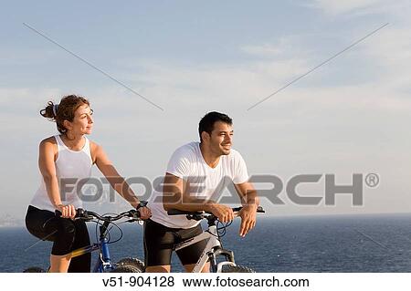 Couple enjoying the views in a cliff with their bikes View Large Photo Image Stock Photo - Couple enjoying the views in a cliff with their bikes. Fotosearch