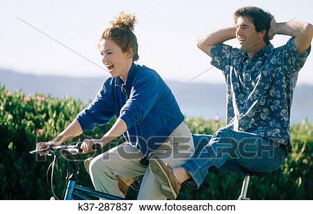 Stock Photo - Couple having fun on tandem cycle on vacation. Fotosearch