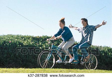 Stock Photo - Couple having fun on tandem cycle on vacation. Fotosearch