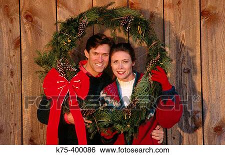 Stock Photograph - Couple holding Christmas wreath for portrait. Fotosearch
