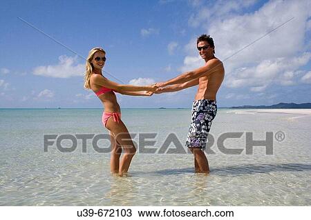 Stock Image - Couple holding hands in the sea. Whitehaven beach, Australia.. Fotosearch