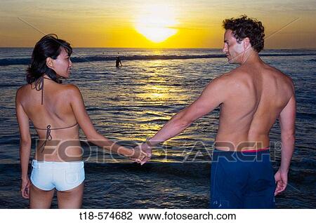 couple holding hands on beach with sunset in the background View Large Photo Image Stock Image - couple holding hands on beach with sunset in the background. Fotosearch