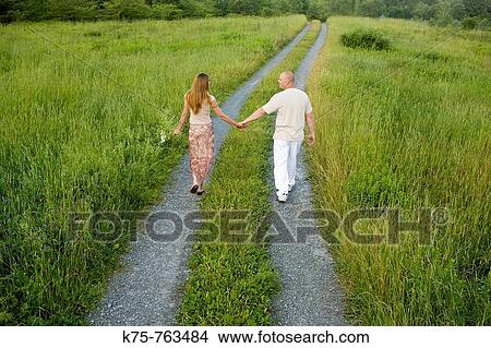 Picture - couple holding hands walking down country road. Fotosearch