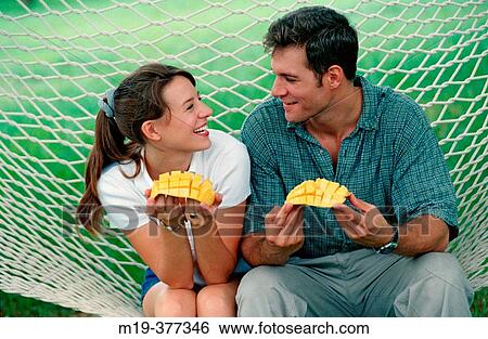 Stock Photograph - couple in a hammock eating mangoes. Fotosearch