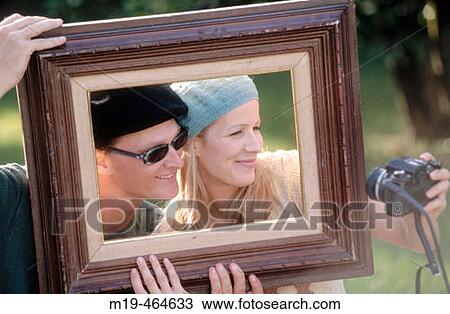 Stock Image - couple in a picture frame taking a photo of themselves. Fotosearch