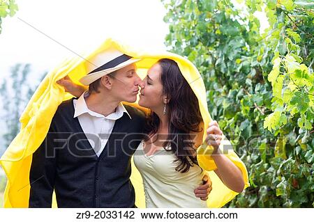 Couple in late twenties kissing under a blanket in the rain while walking through a vineyard in the Winelands, Western Cape, Stellenbosch, South Africa. View Large Photo Image Stock Image - Couple in late twenties kissing under a blanket in the rain while walking through a vineyard in the Winelands, Western Cape, Stellenbosch, South Africa.. Fotosearch