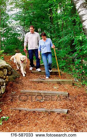 Stock Image - Couple (in mid 40? s) hiking along suburban trail with golden retriever dog.. Fotosearch