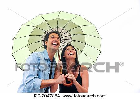 Picture - Couple in their 30's smiling under umbrella.. Fotosearch