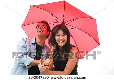 Stock Image - Couple in their 30's smiling under umbrella.. Fotosearch